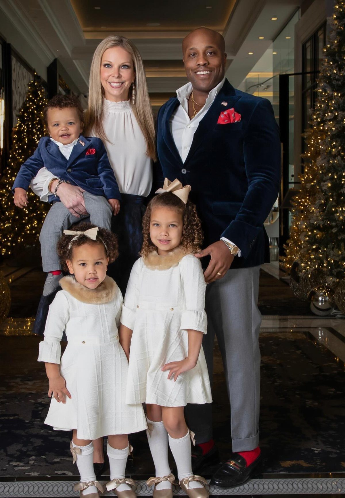 A smiling family of five posing together in elegant, festive clothing indoors.