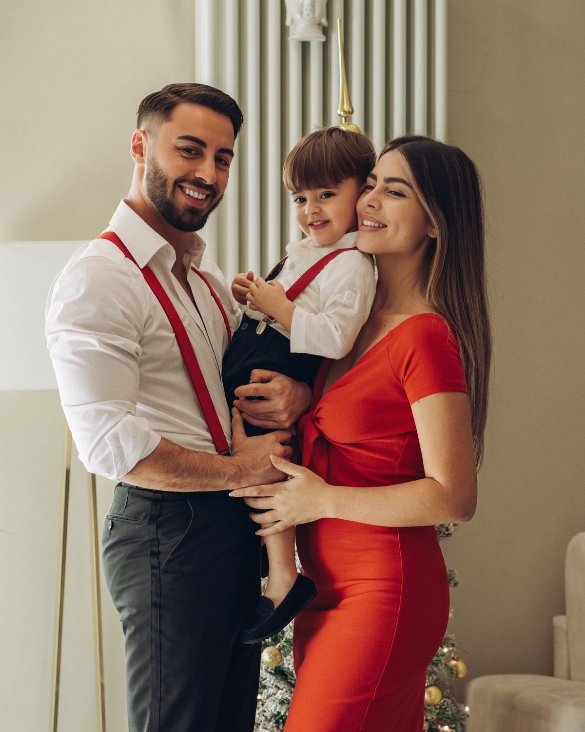 A smiling family posing together, featuring a man in red suspenders and a woman in a red dress.