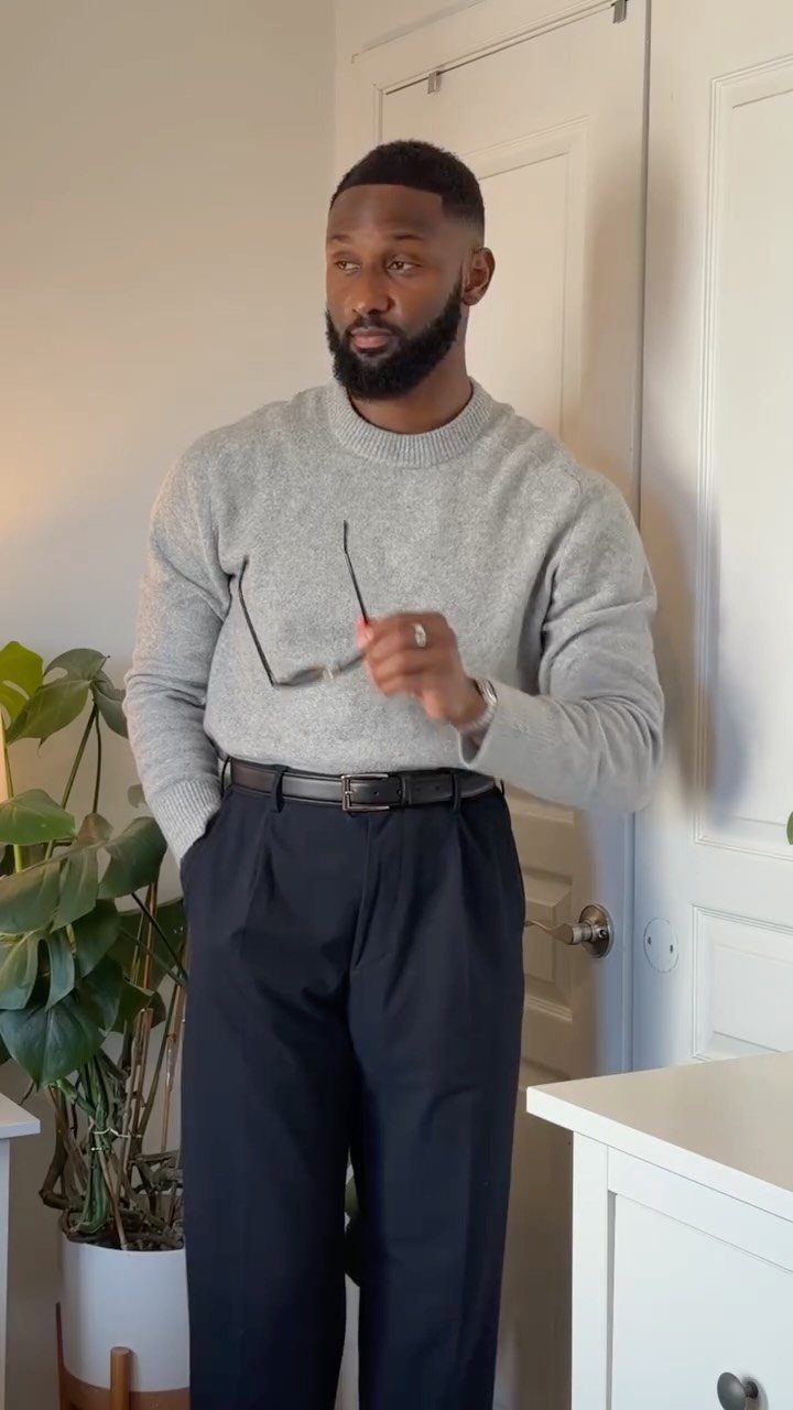 A man wearing a grey sweater and black trousers standing in a room.