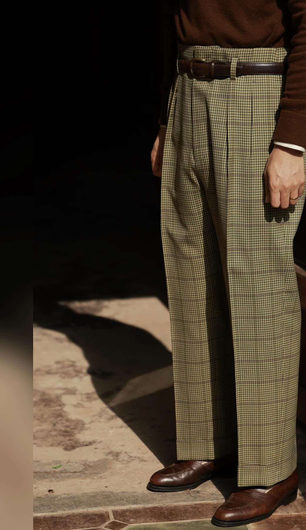 Person wearing high-waisted checkered trousers with a brown belt and leather shoes.