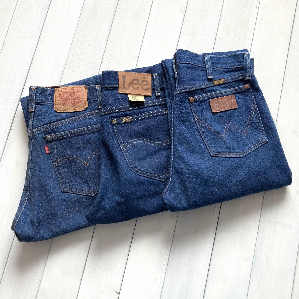 Three pairs of folded blue denim jeans resting on white wooden planks.