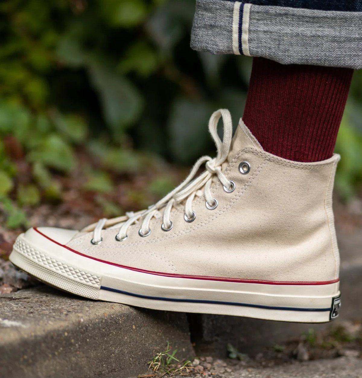 Cream high-top canvas sneakers with red and blue stripes worn with burgundy socks.