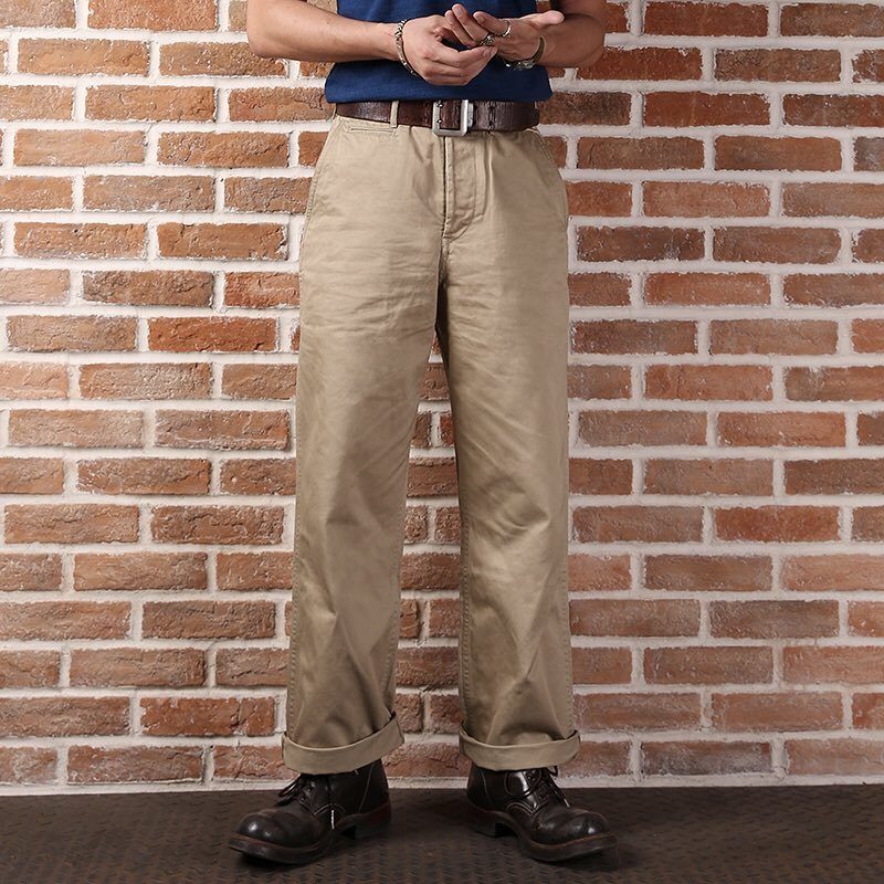 A person wearing tan khaki trousers, a blue shirt, and dark brown leather boots.