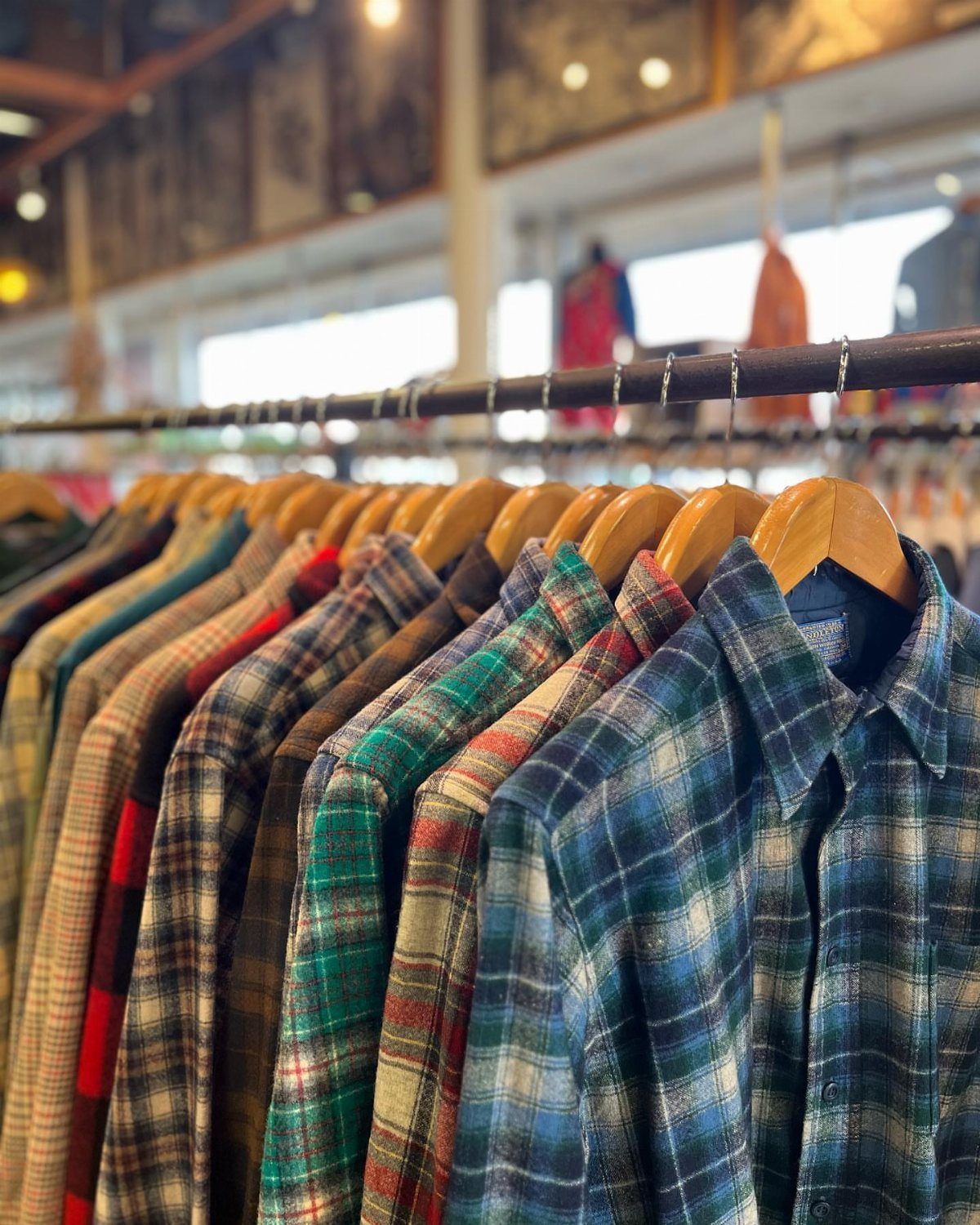 Plaid flannel shirts in various colors hanging on wooden hangers on a clothing rack.