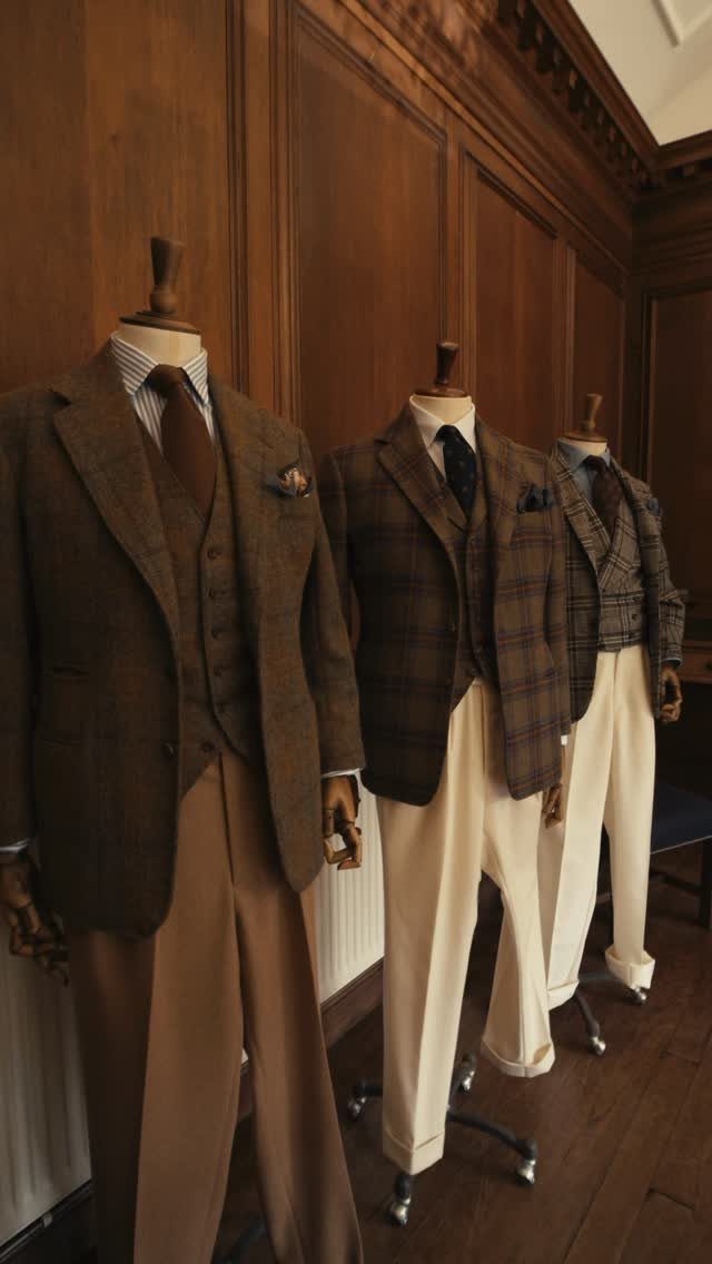 Three mannequins wearing classic American style wool blazers, waistcoats, ties, and trousers against wood paneling.