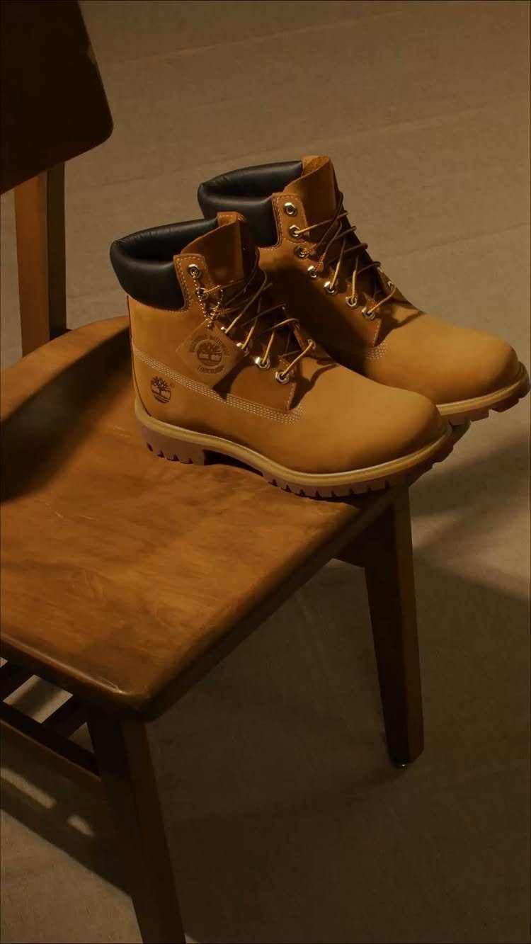 Tan leather work boots with yellow laces resting on a wooden chair seat.