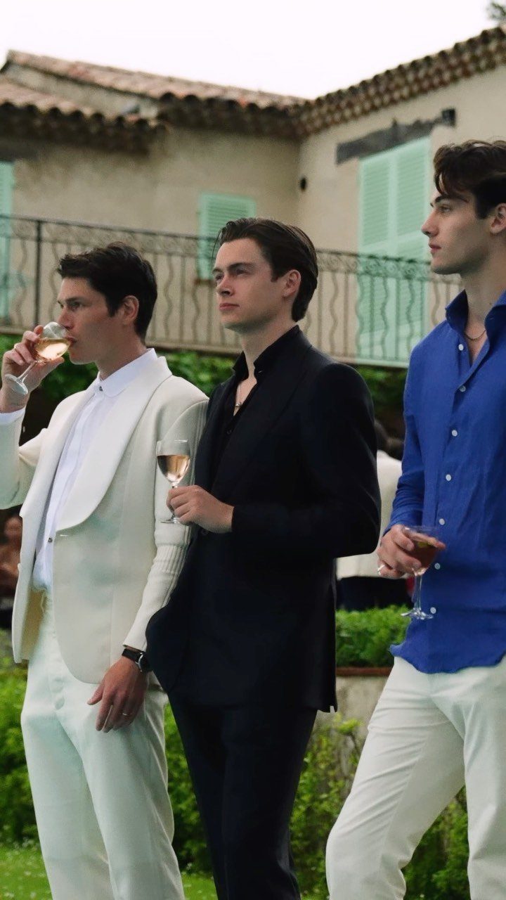 Three men dressed in stylish semi-formal attire standing together outdoors near a building.
