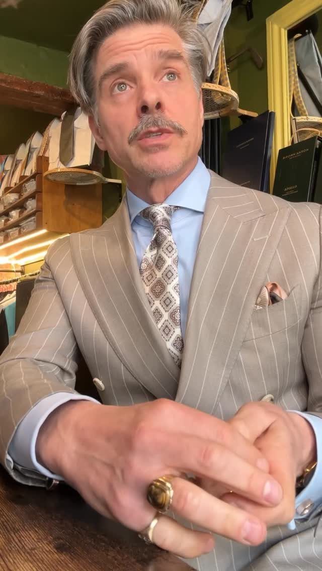 A man with a mustache wearing a pinstripe suit, light blue shirt, and patterned tie.