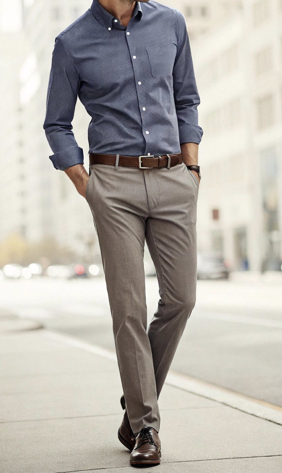 Man walking on a city sidewalk wearing a blue button-up shirt and tan trousers.