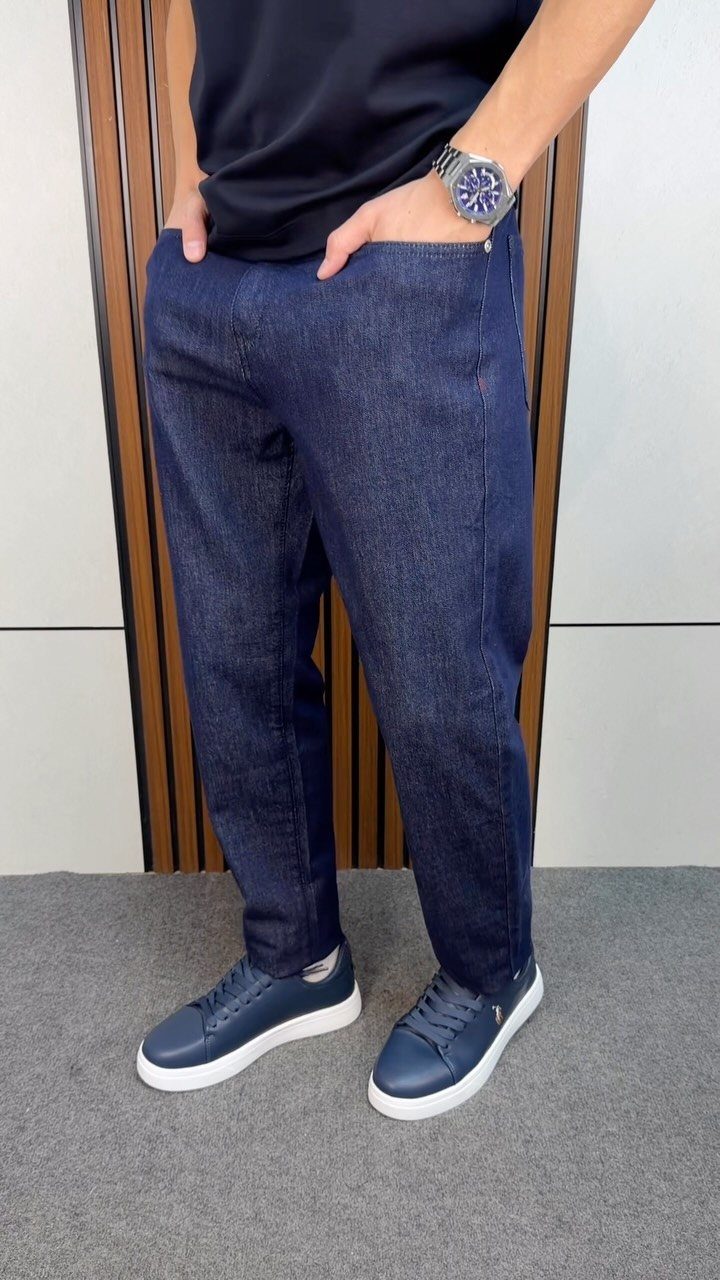 A person wearing dark navy blue denim trousers, a black t-shirt, and navy sneakers.