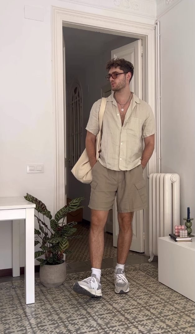 A man in a beige shirt and tan shorts standing in a room with a tote bag.