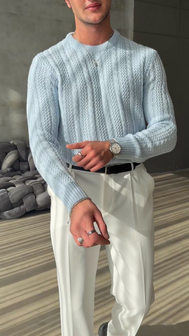 Man wearing a light blue textured sweater and white trousers with a black belt.