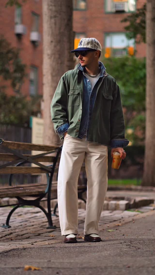 A man wearing a green utility jacket over a denim shirt and cream trousers.