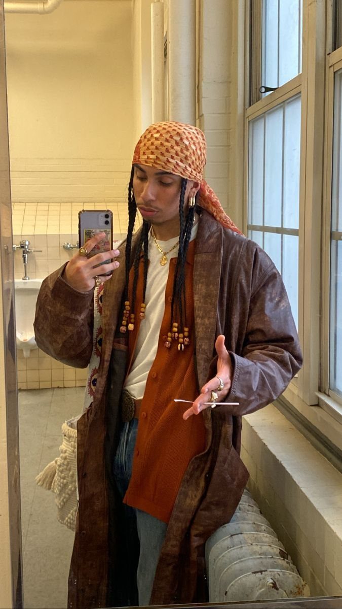 Man in a long brown leather coat and orange shirt taking a mirror selfie.