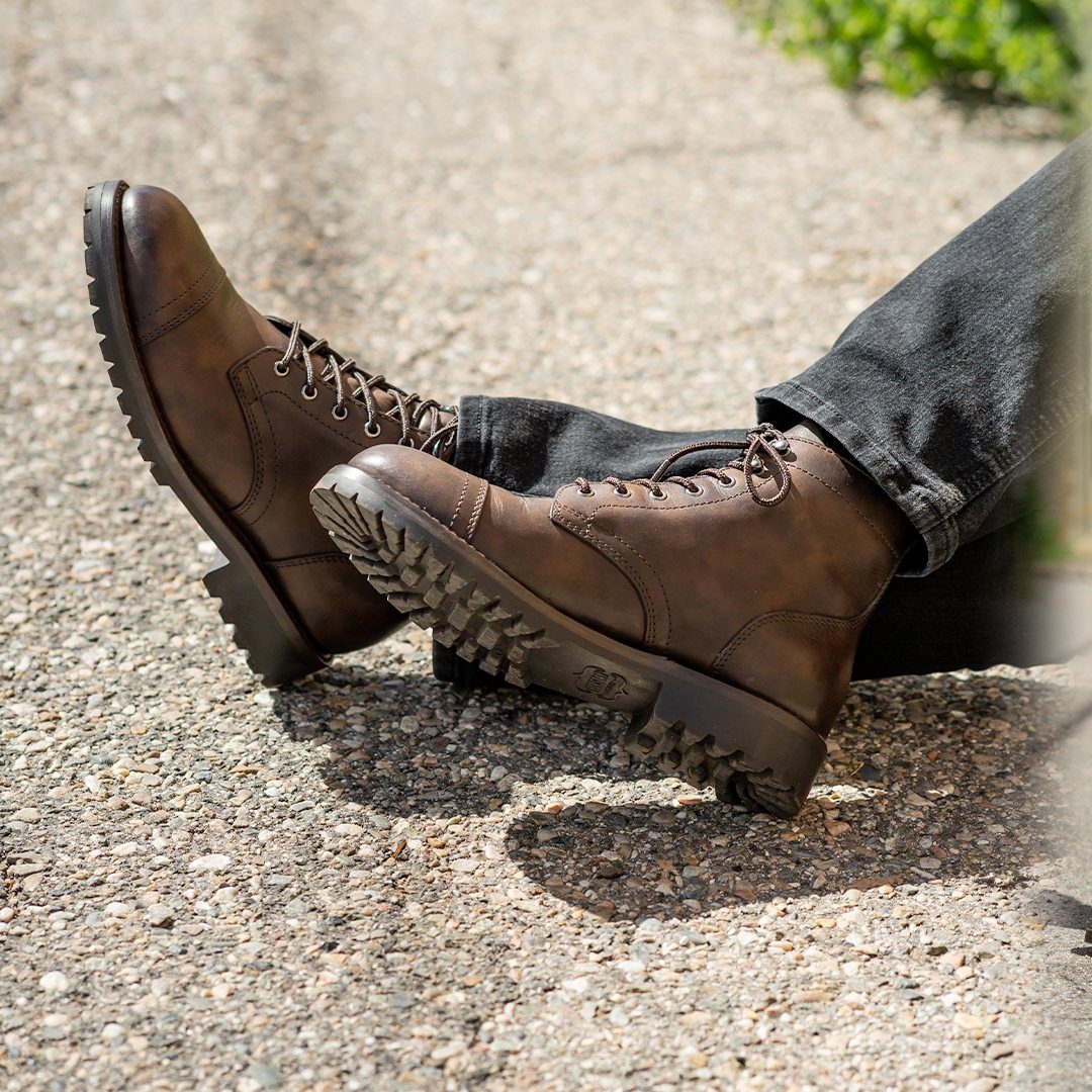 Brown leather lace-up boots worn with dark denim jeans on a concrete surface.