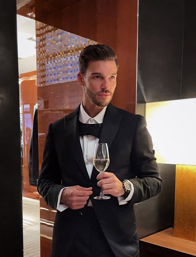 Man in a black shawl lapel dinner suit holding a glass of champagne.
