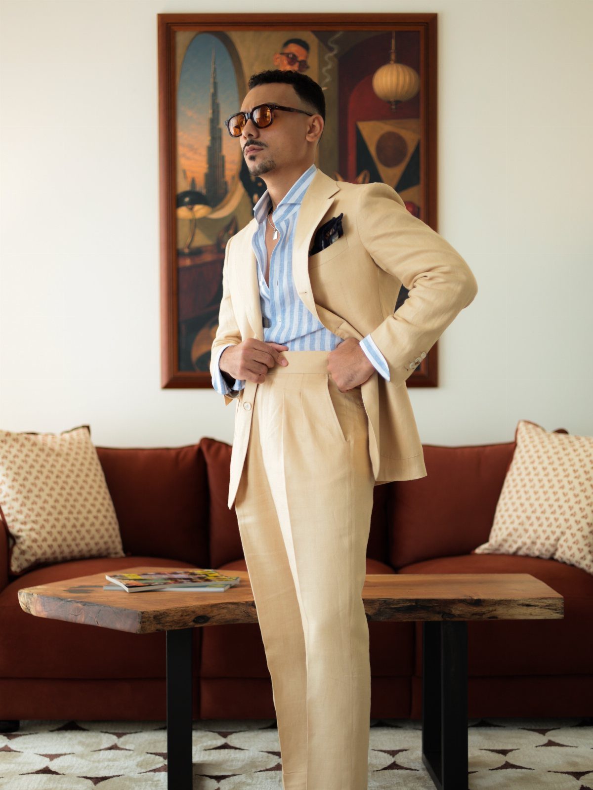 Man in a tan linen suit and striped shirt posing in a living room.