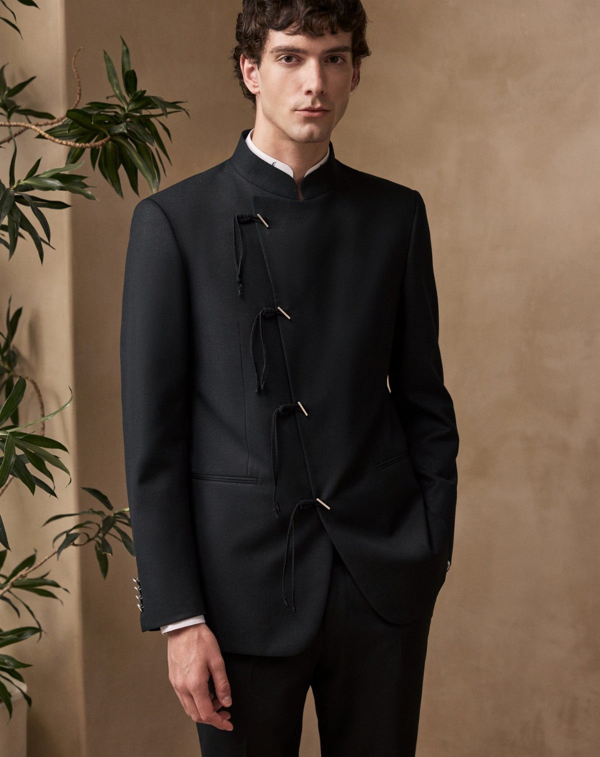 Man wearing a dark navy blue Mandarin collar suit jacket with unique side fastenings.