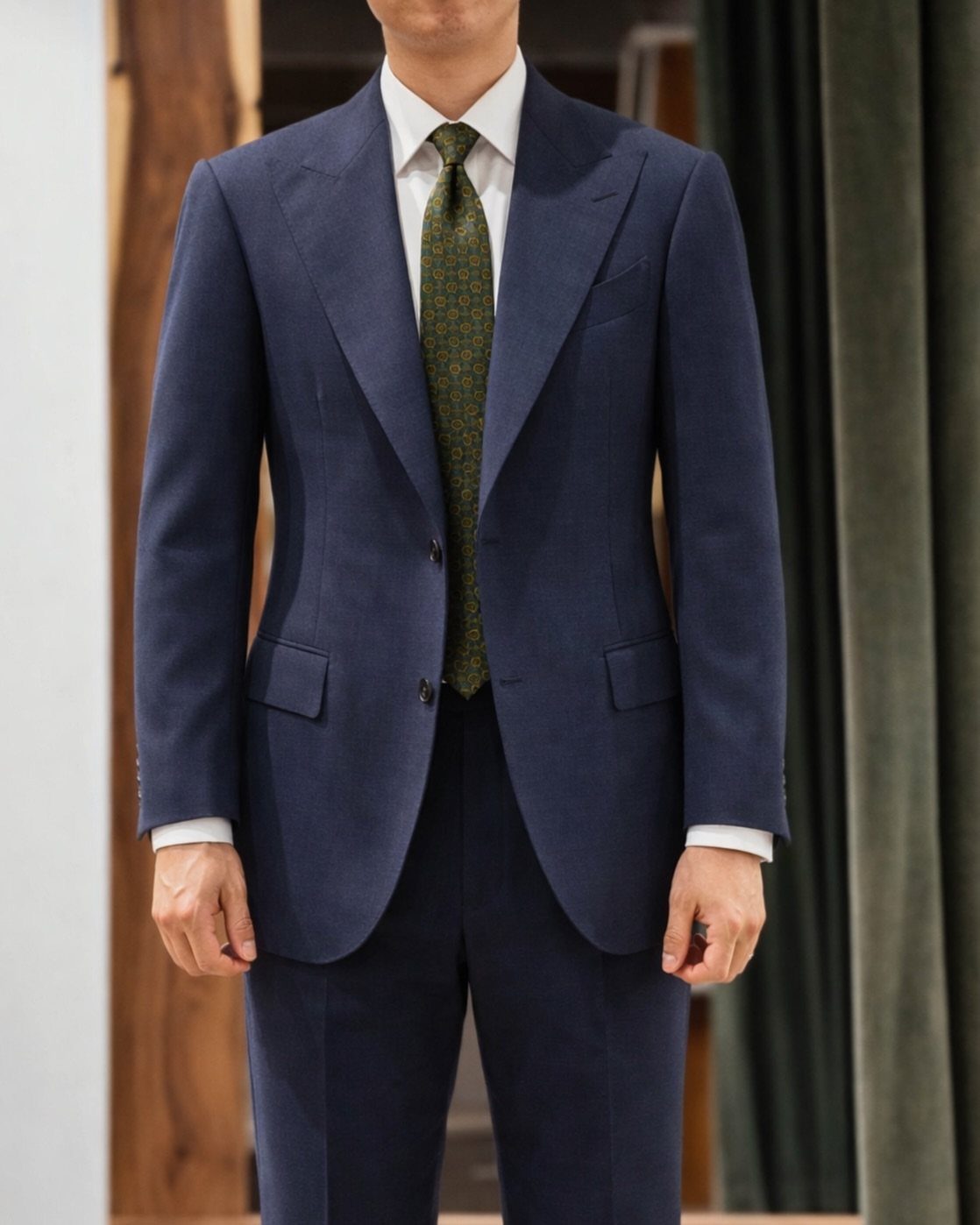 Man wearing a navy blue single-breasted suit with a white shirt and green patterned tie.