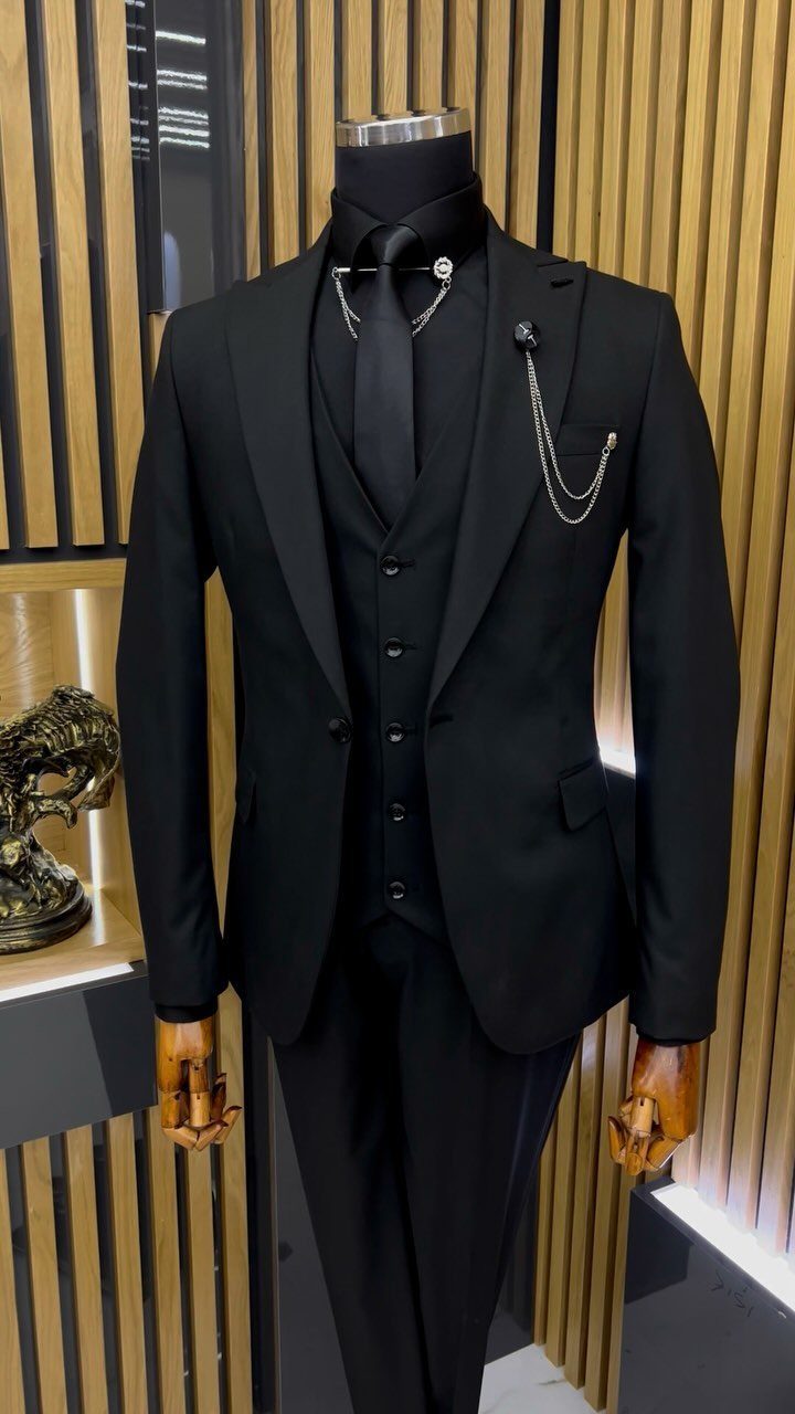 Black three-piece suit with silver chains displayed on a mannequin against a wooden slatted background.