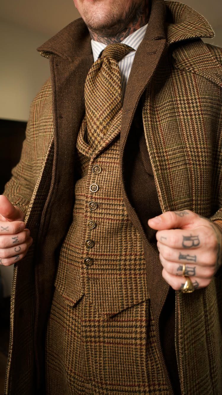 Man wearing a brown plaid tweed three-piece suit with a matching tie and heavy overcoat.