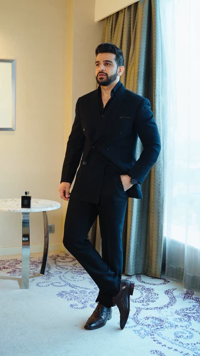 Man in a black formal suit and brown leather shoes posing in a room.
