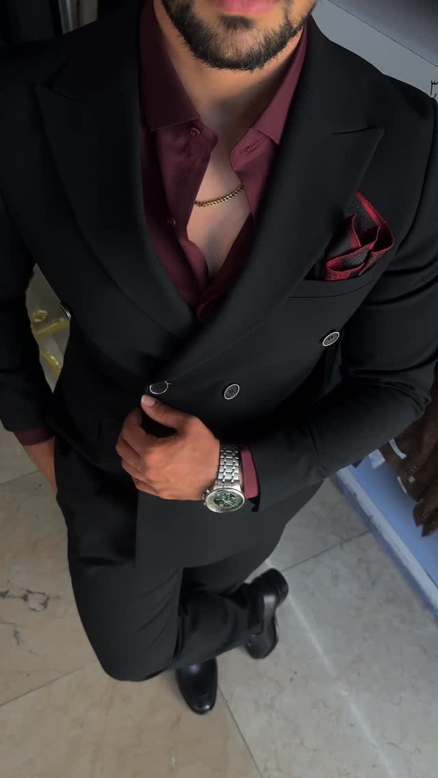 Man in a black double-breasted suit and burgundy shirt standing on a tiled floor.