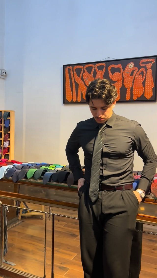 A man wearing a black dress shirt and a black necktie standing in a clothing store.