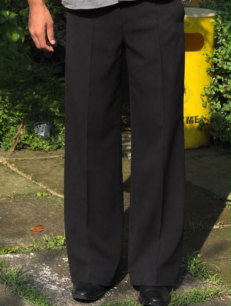 Black wide-leg tailored trousers worn by a person standing on a stone path outdoors.