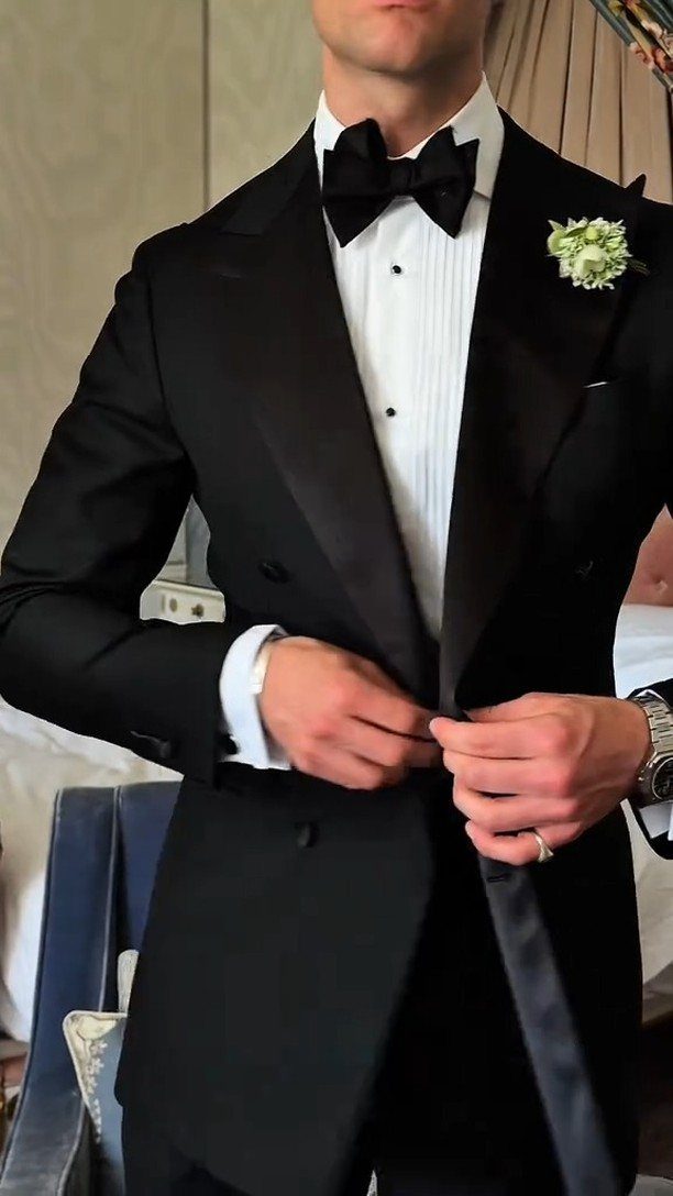 Man in a black tuxedo with a white shirt and black bow tie adjusting his jacket.