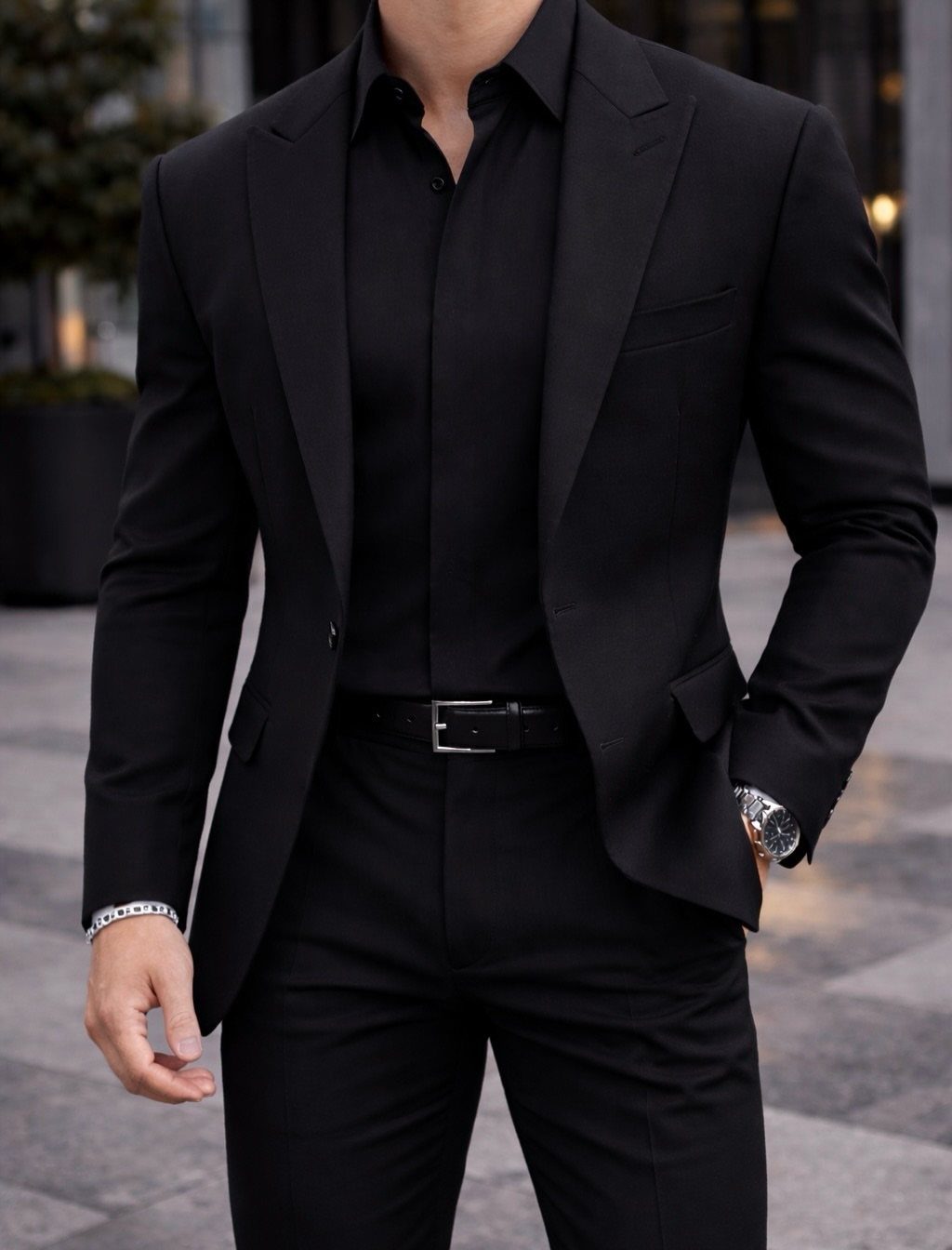 Man wearing a sharp black two-piece suit with a black dress shirt and leather belt.