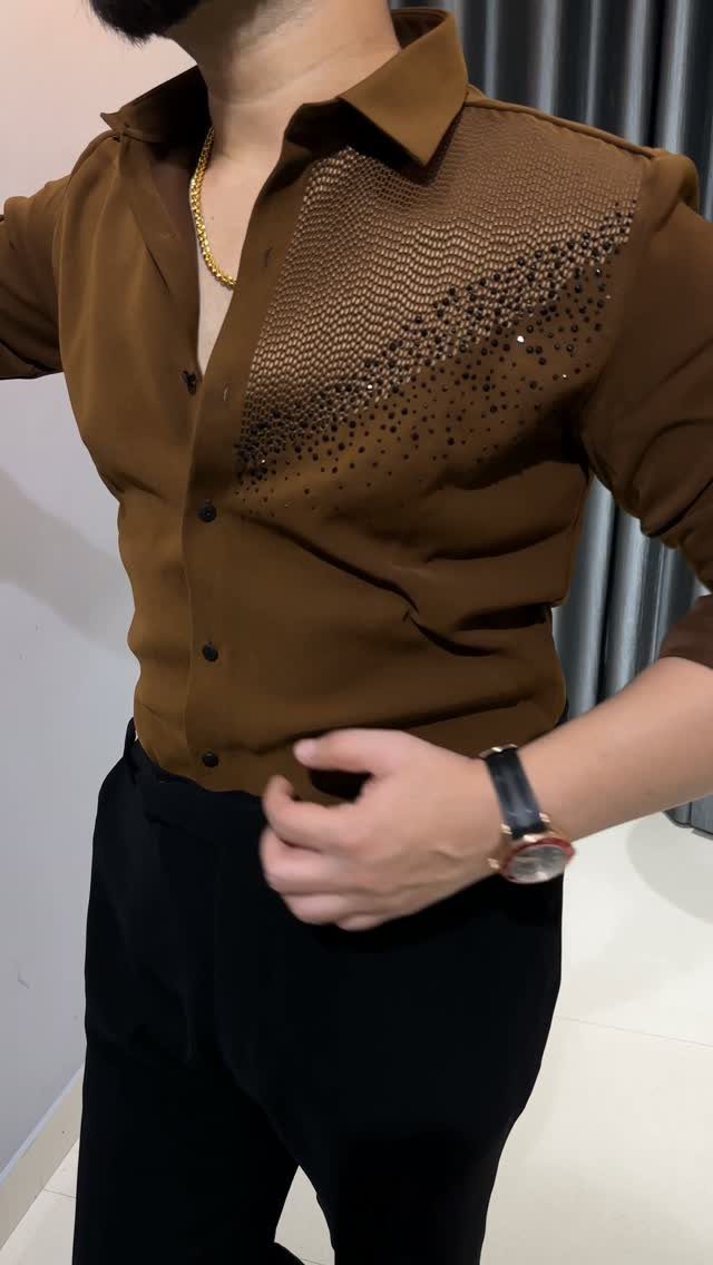 Man wearing a brown embellished button-down shirt and black trousers with a gold chain.
