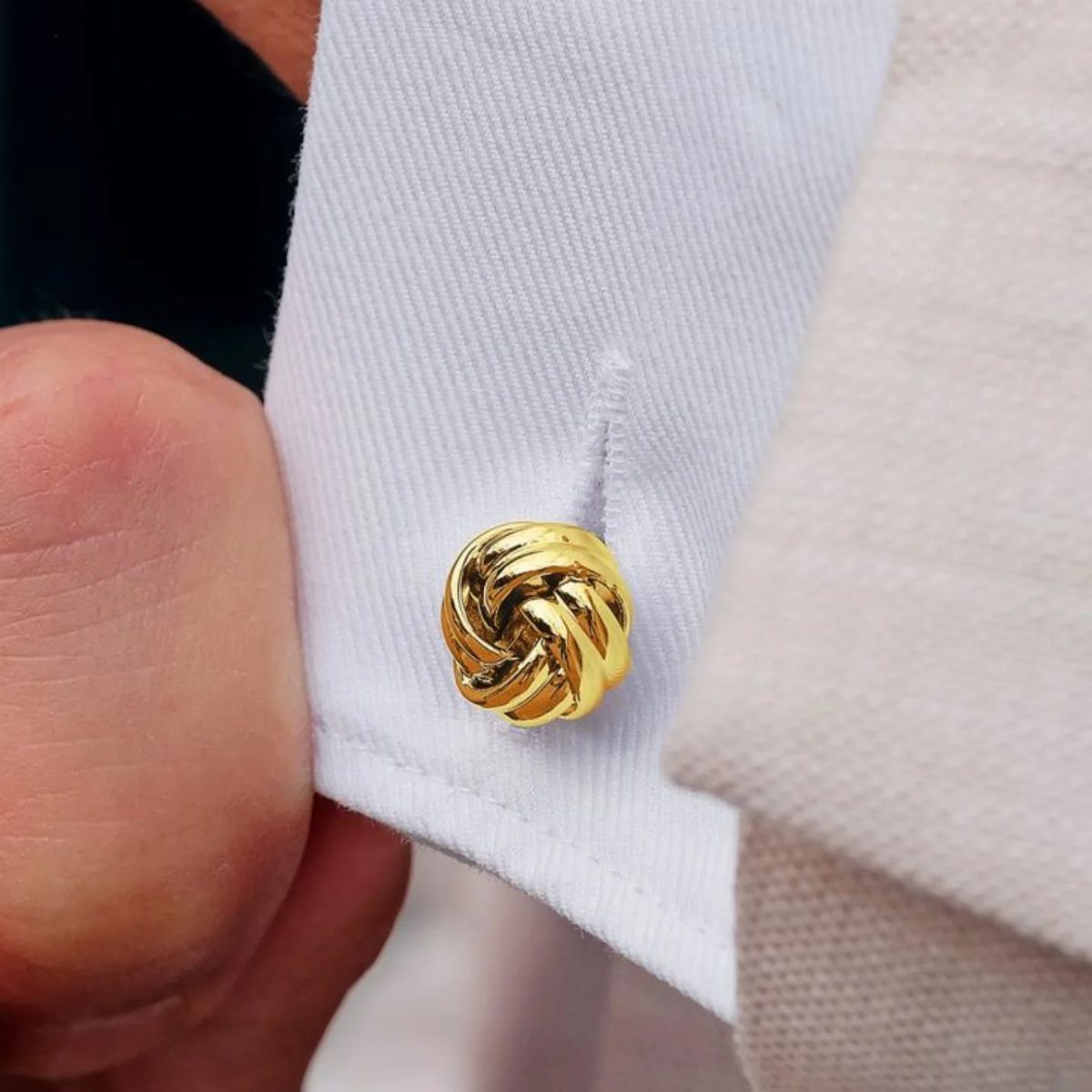 Gold knot-shaped cufflink fastened to a white formal shirt cuff.