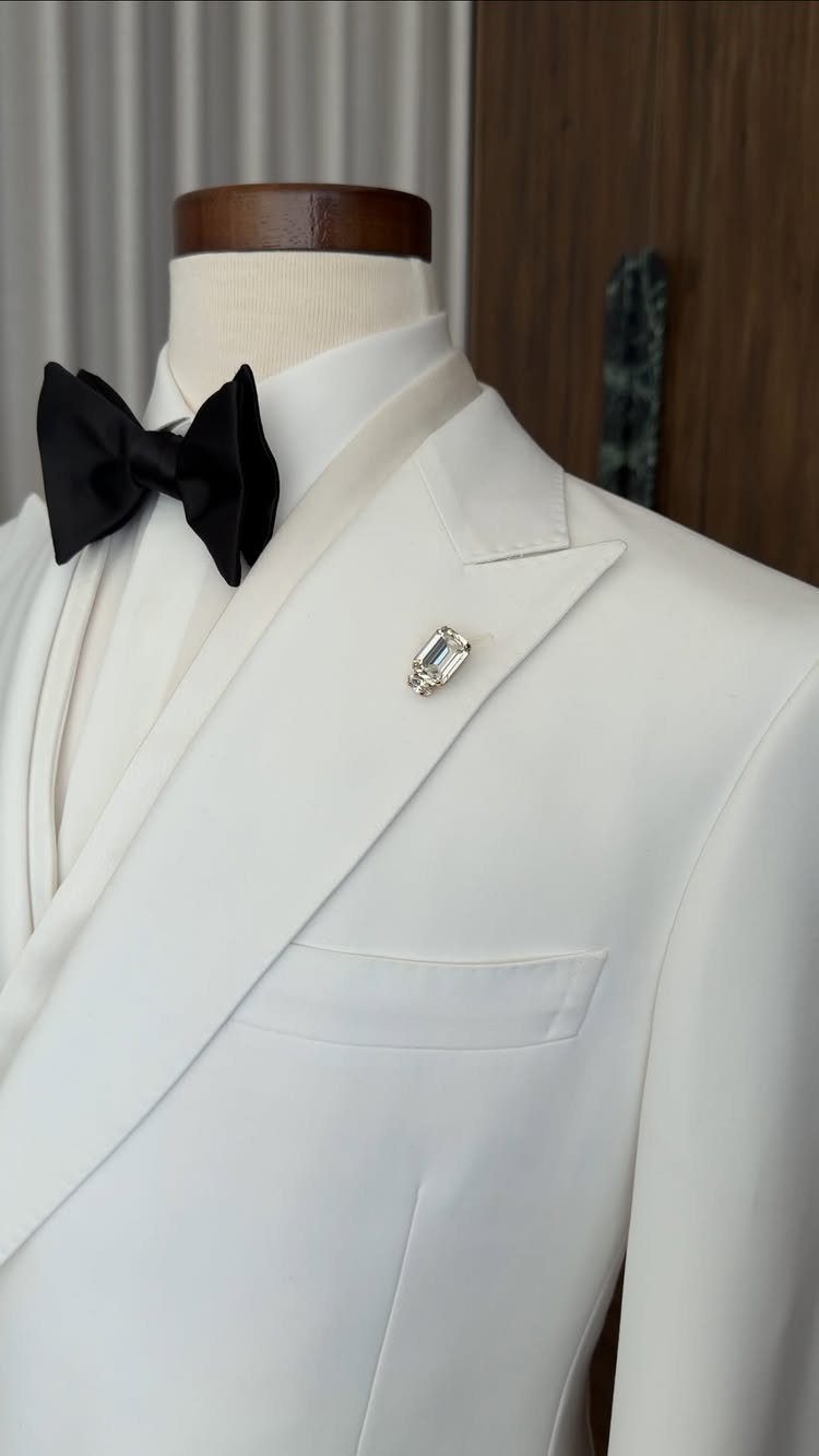 White tuxedo jacket with a black bow tie and lapel pin on a mannequin.