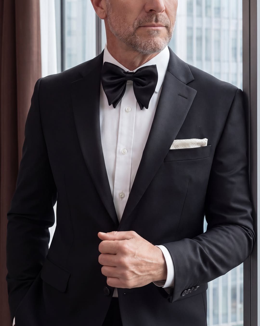 Man in a black tuxedo and white shirt wearing a black silk bow tie.