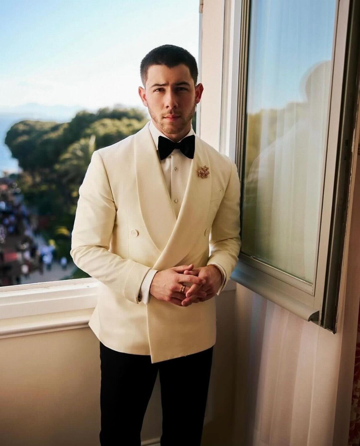 Man in a cream tuxedo jacket and black bow tie standing on a balcony.