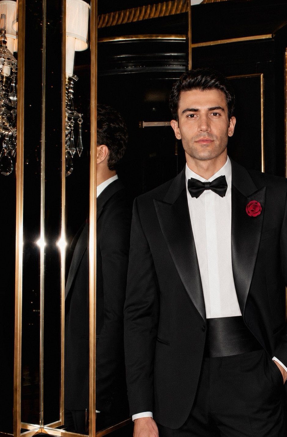 Man in a black tuxedo with a white shirt and black bow tie posing in a dark room.