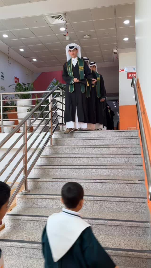A male graduate in a black gown and green stole standing atop a staircase.