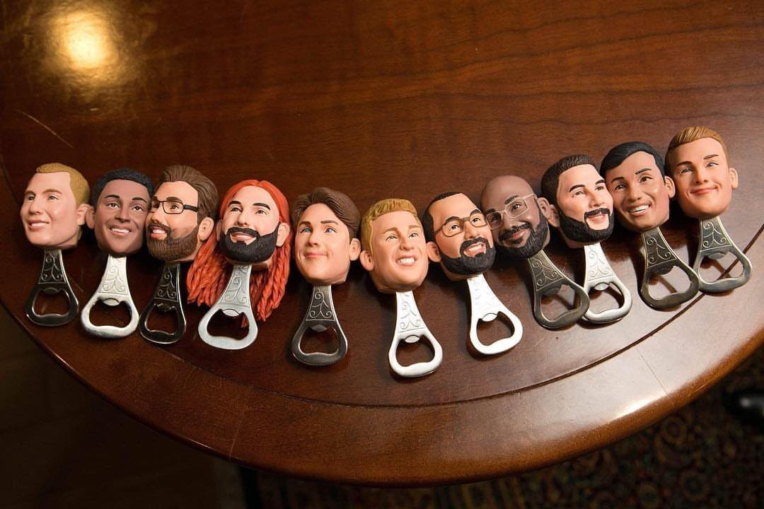 Customized 3D-printed head bottle openers arranged in a row on a wooden surface.