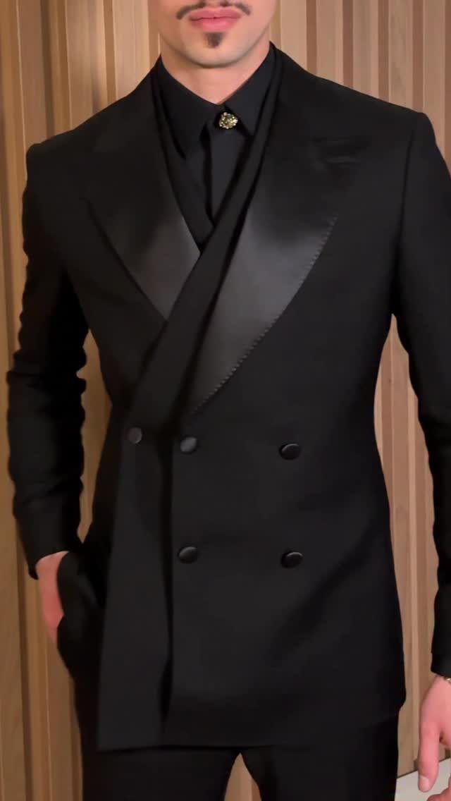 A man wearing a tailored black double-breasted suit with satin lapels and a black shirt.