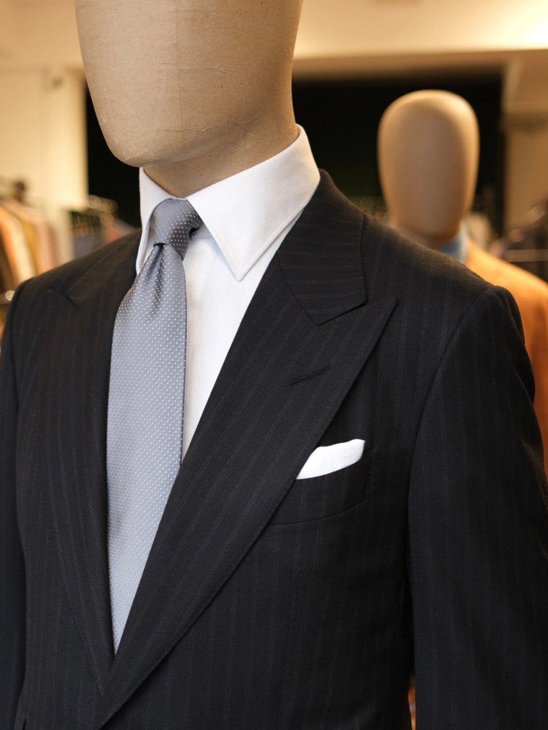 Mannequin wearing a black pinstripe suit, white shirt, and grey tie with a pocket square.