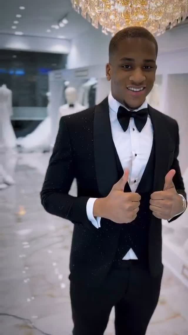 Smiling man in a black tuxedo with a bow tie giving two thumbs up.