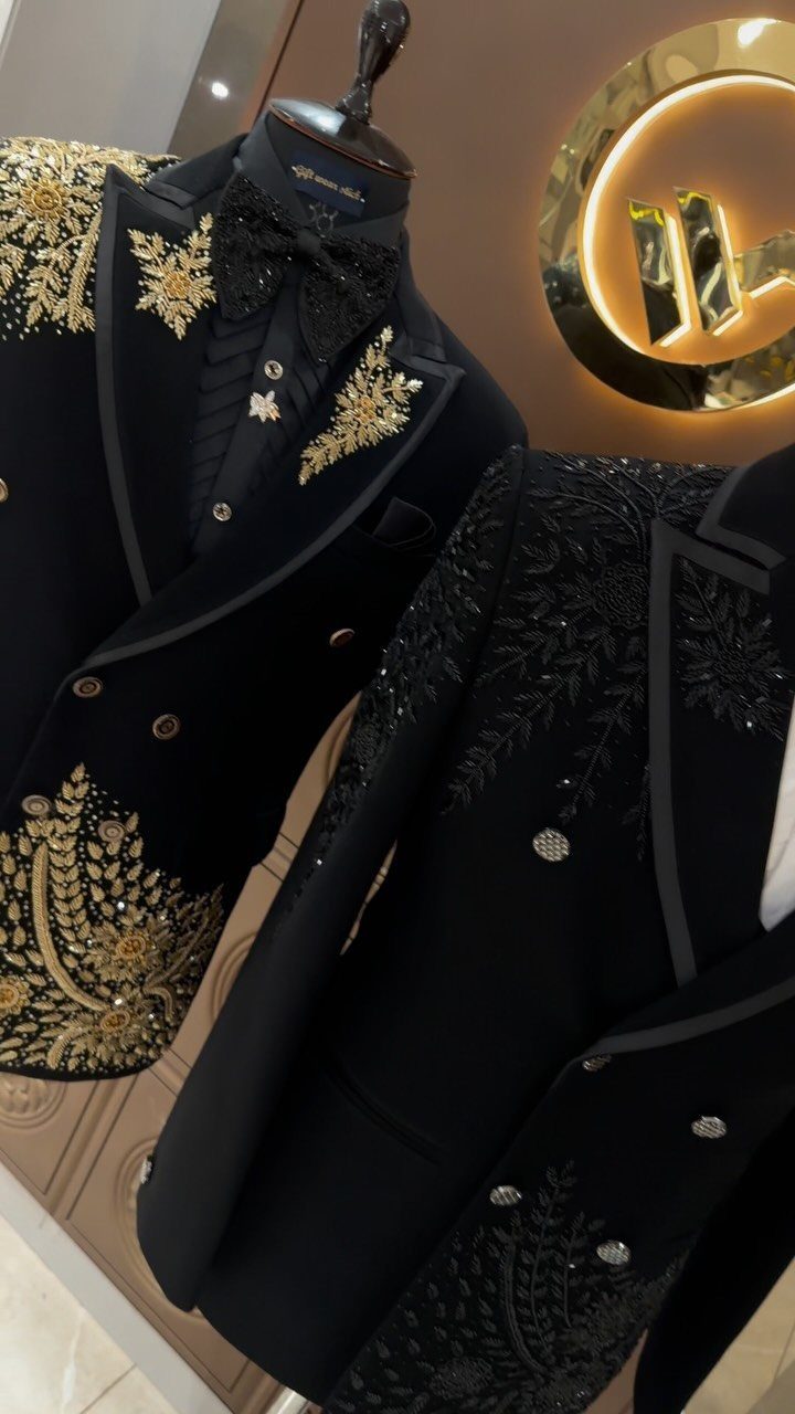 Two black embroidered formal jackets displayed on mannequins with gold and black decorative patterns.