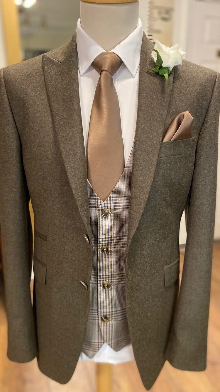 A brown wool suit with a patterned waistcoat, tan tie, white rose boutonniere, and pocket square.