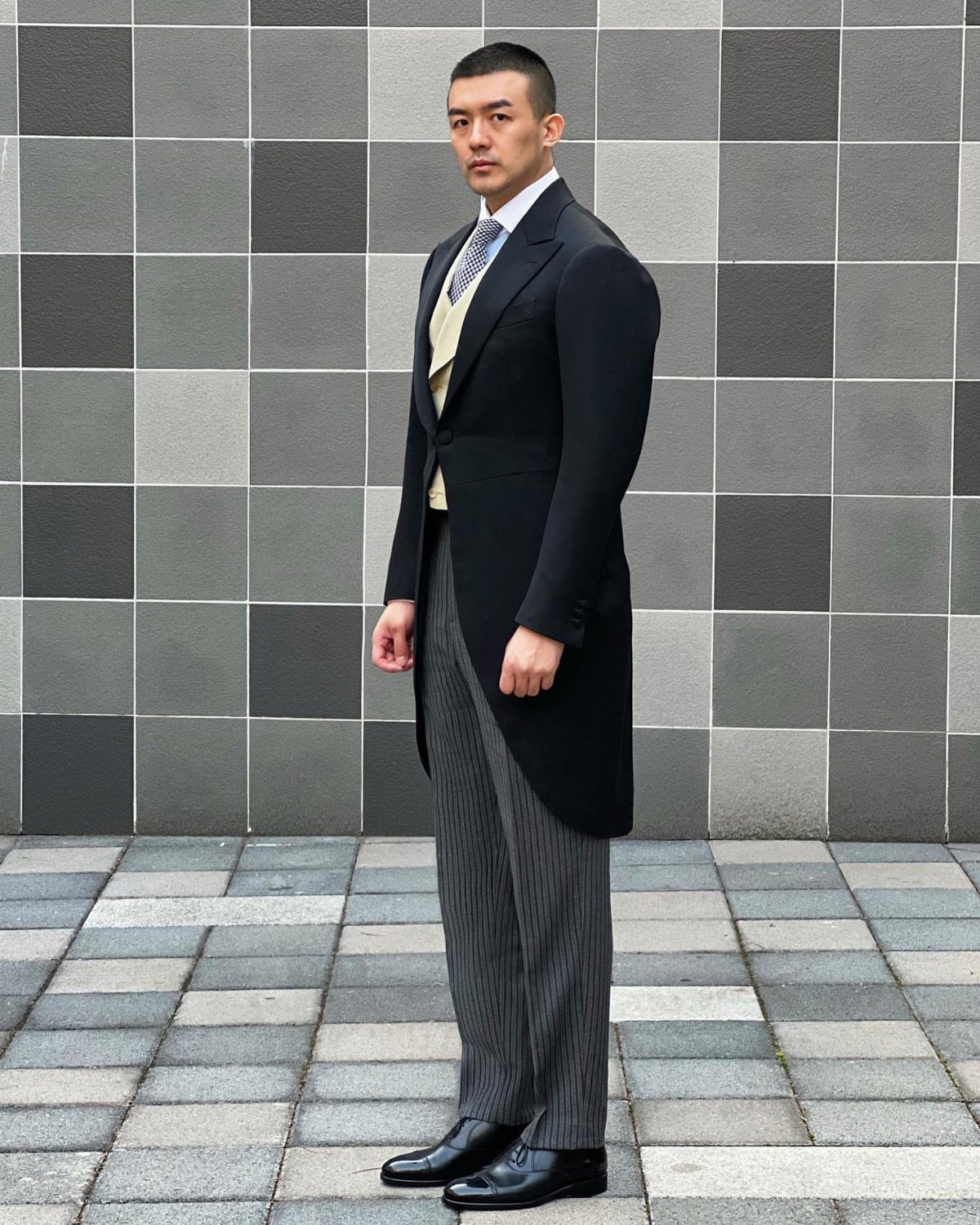A man posing in a black morning coat, yellow waistcoat, and striped trousers.