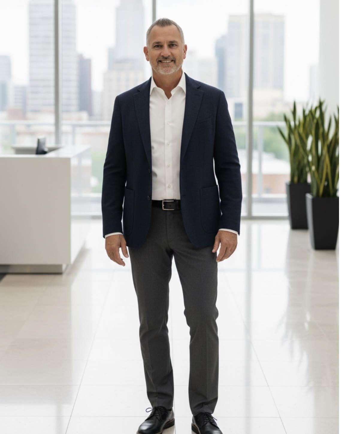 Man in a navy blazer, white shirt, and grey trousers standing in a modern office.