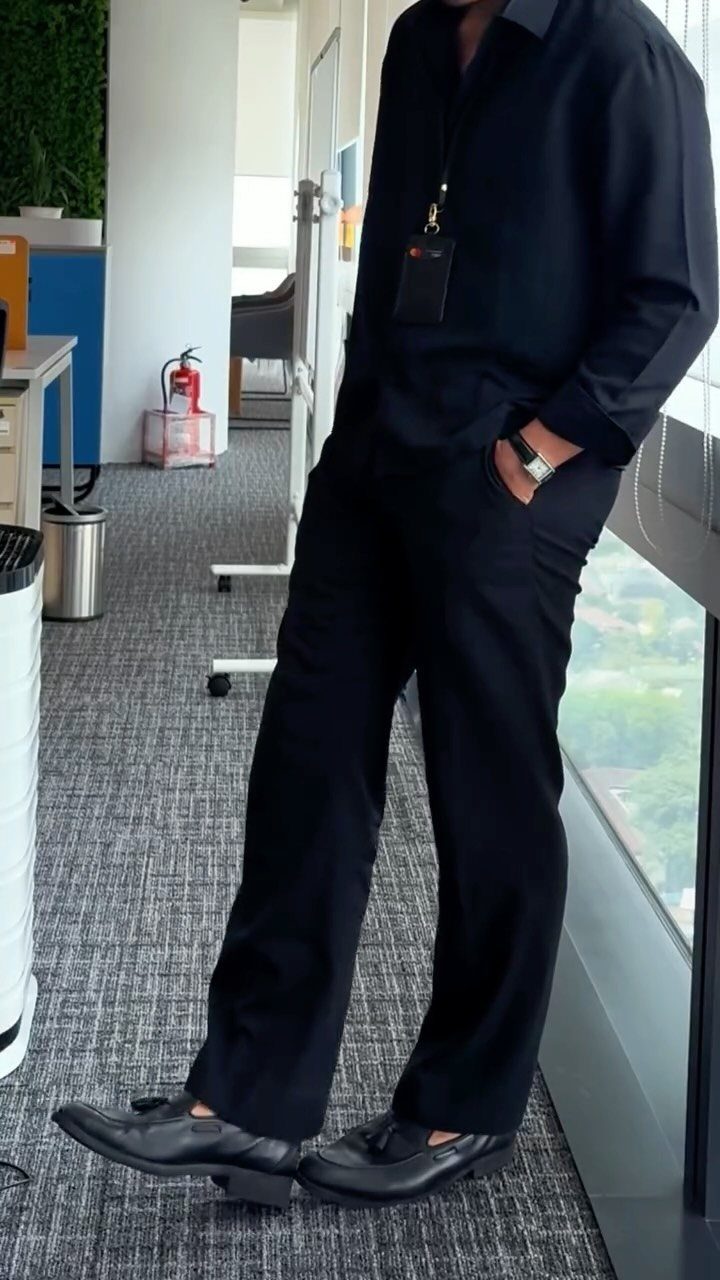 Man in an all-black business casual outfit standing in a modern office space.