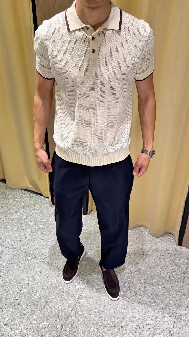 Man wearing a cream textured polo shirt with dark trim and navy trousers.