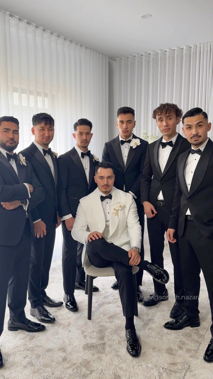 Seven men posing in formal black and white tuxedos for a wedding group portrait.