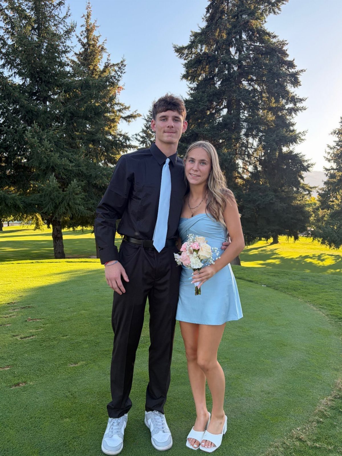 A young man in a black shirt and tie posing with a woman in a blue dress.